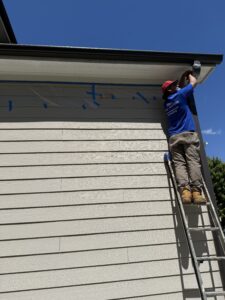 Man on ladder painting a house exterior under clear sky.
