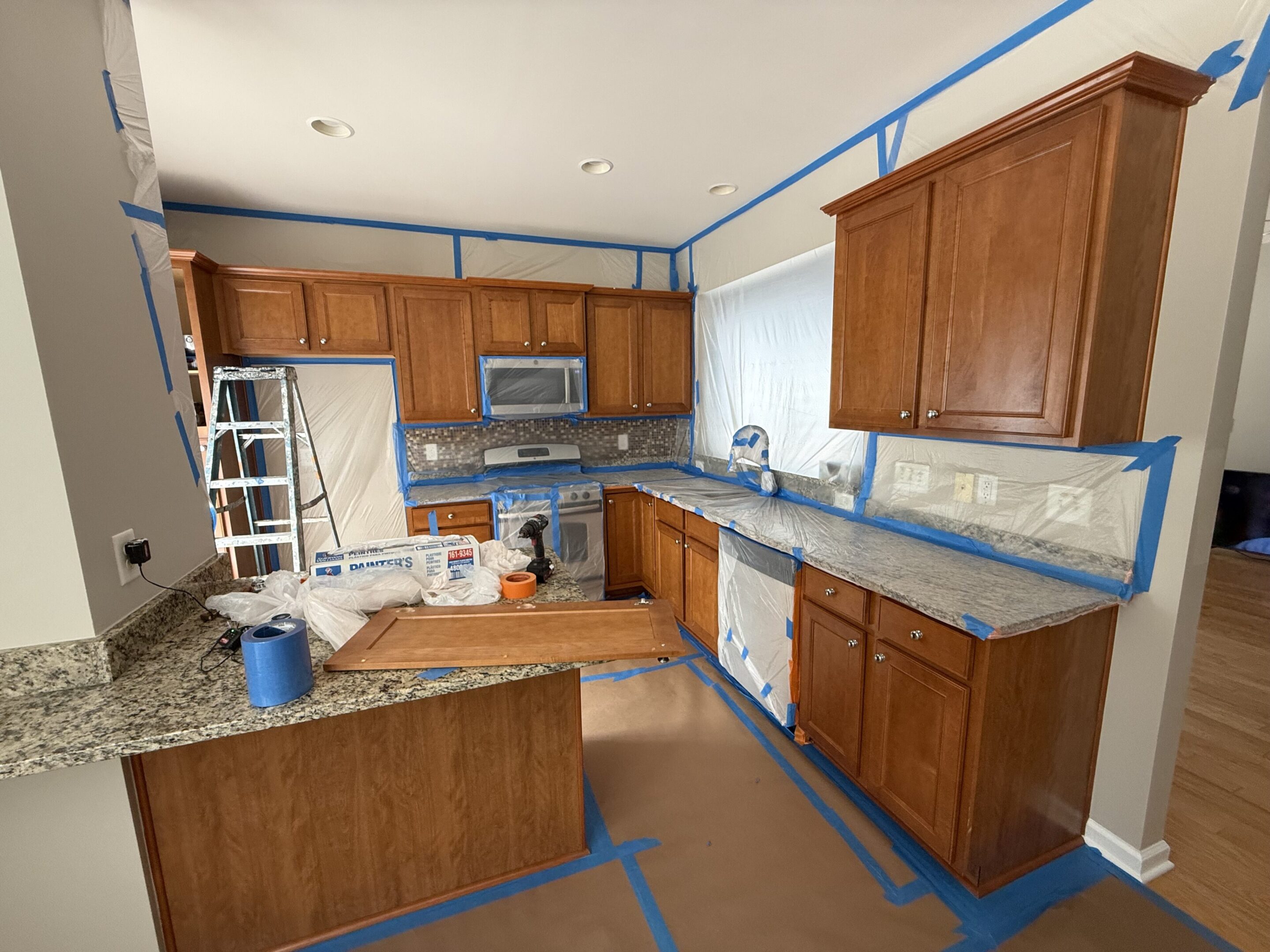 Kitchen undergoing renovation with wooden cabinets and taped floors.