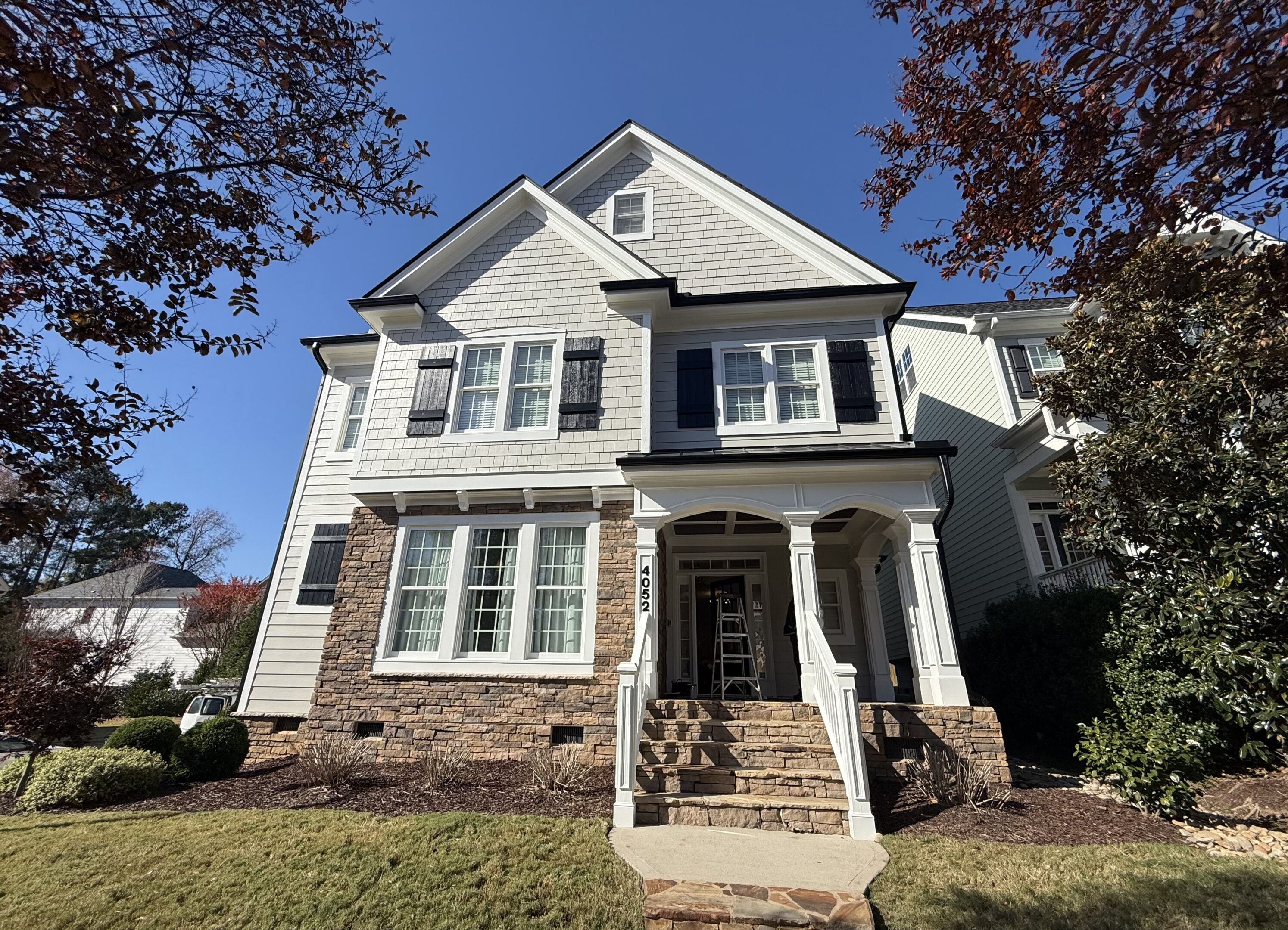 Elegant two-story house with stone and siding exterior under a clear blue sky.
