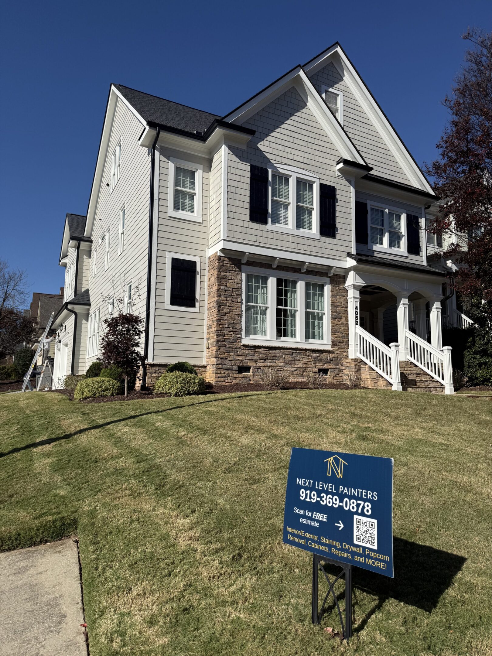 Two-story house with stone and siding exterior, for sale sign in yard.