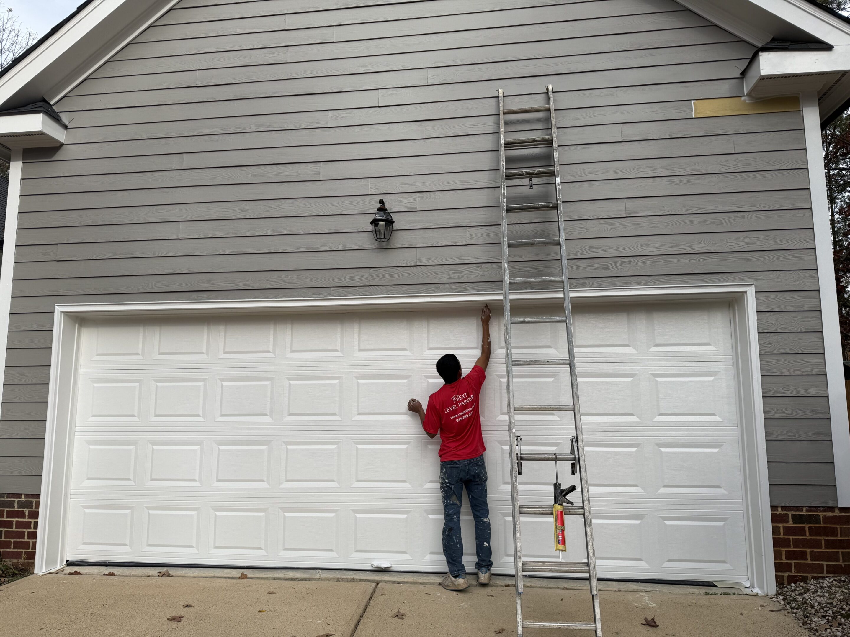 Child reaching up to a wall with a tall ladder beside him.