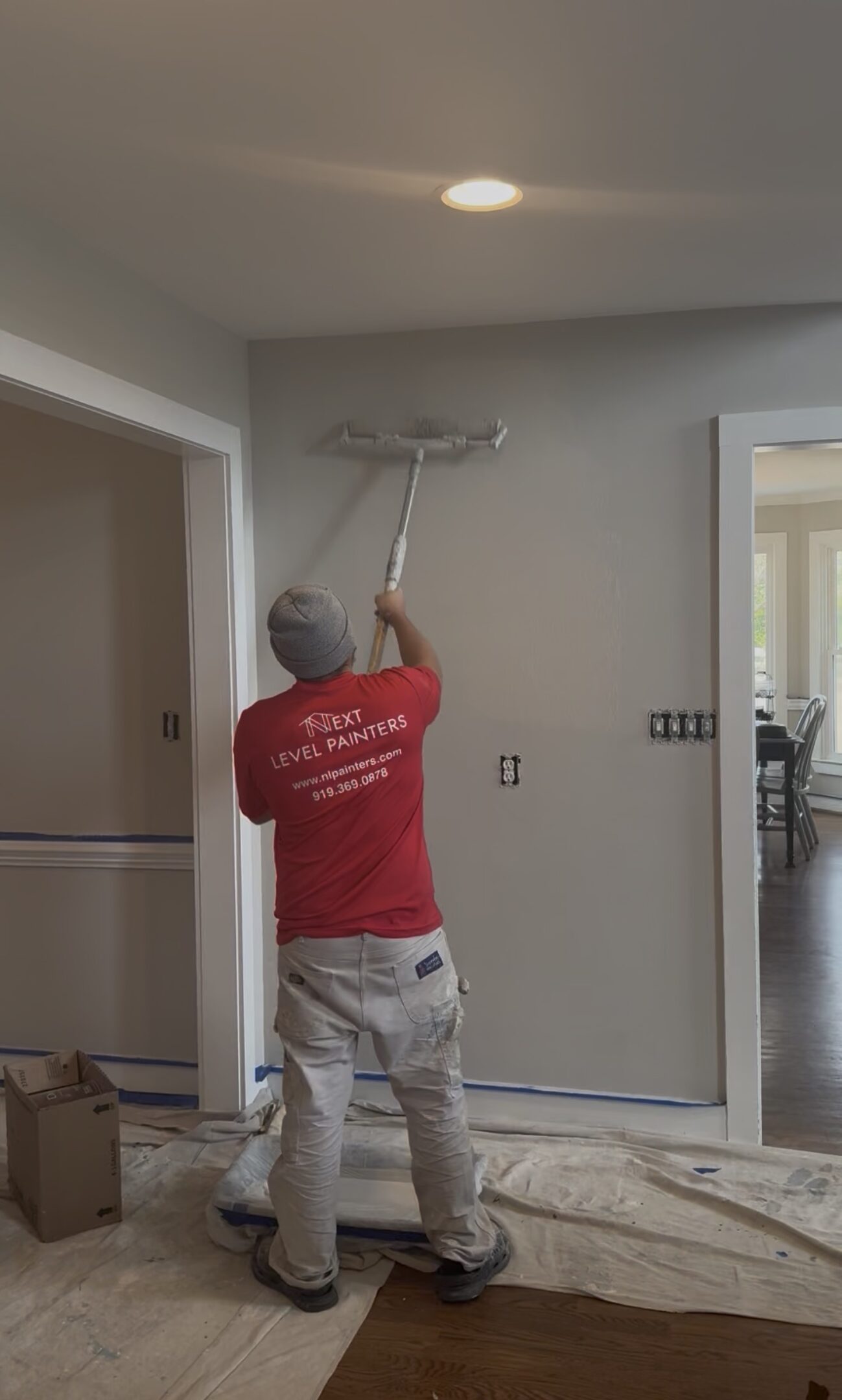 Worker painting a wall with a roller in a residential room.