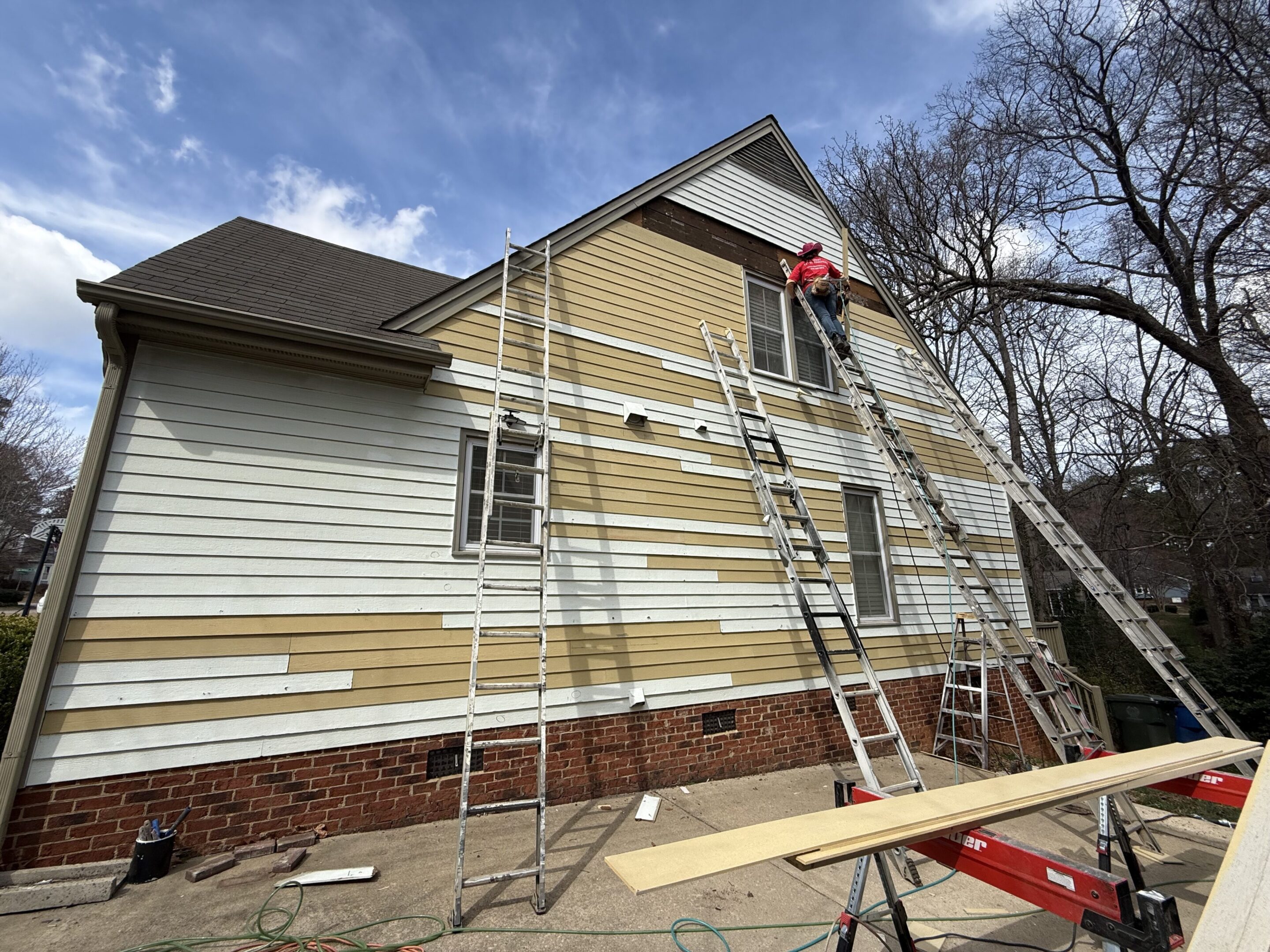 A person working on siding installation on a house using ladders and scaffolding.