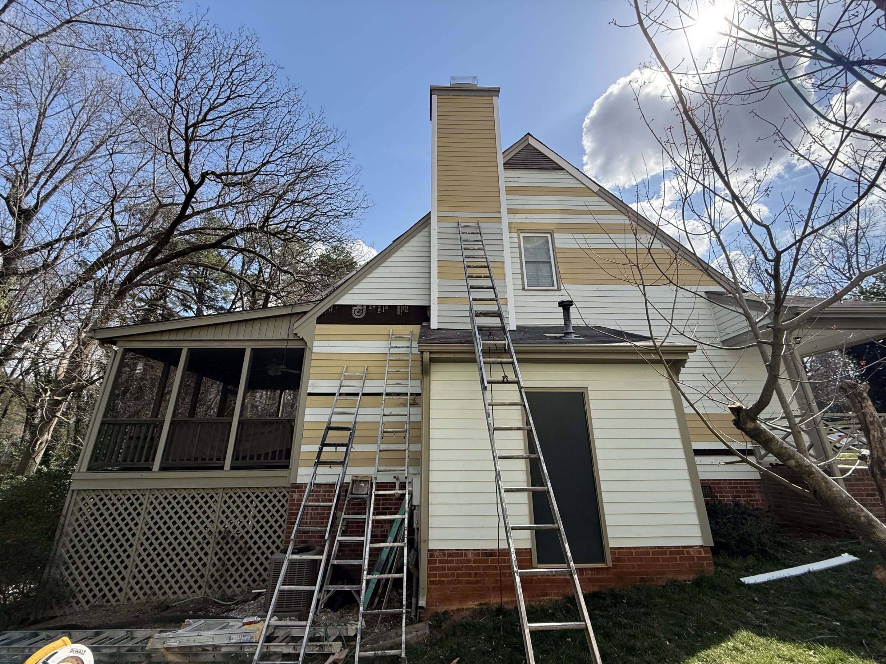 Two ladders leaning against a house with a tall chimney under a partly cloudy sky.