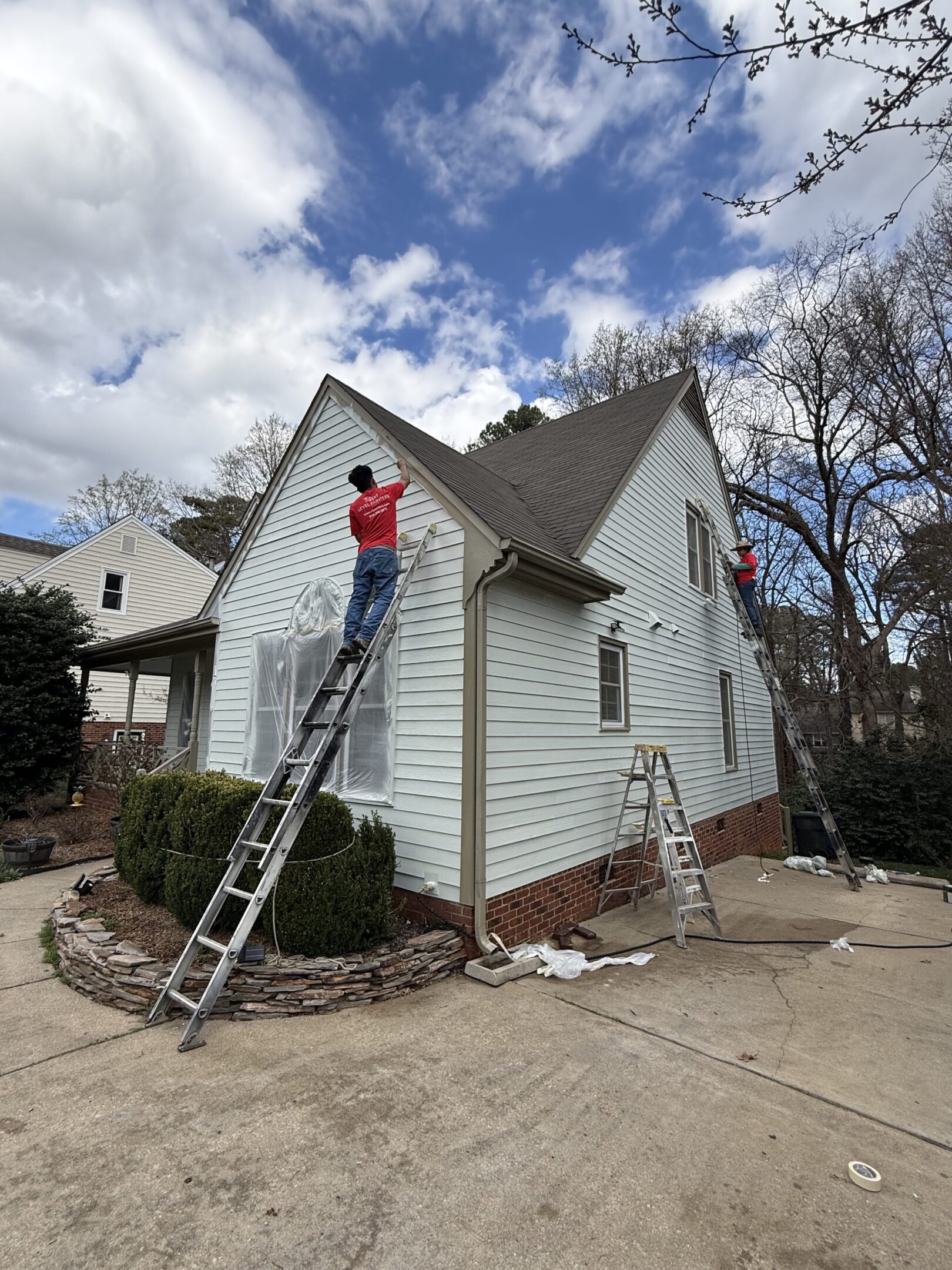 Two workers on ladders painting the exterior of a white house on a clear day.