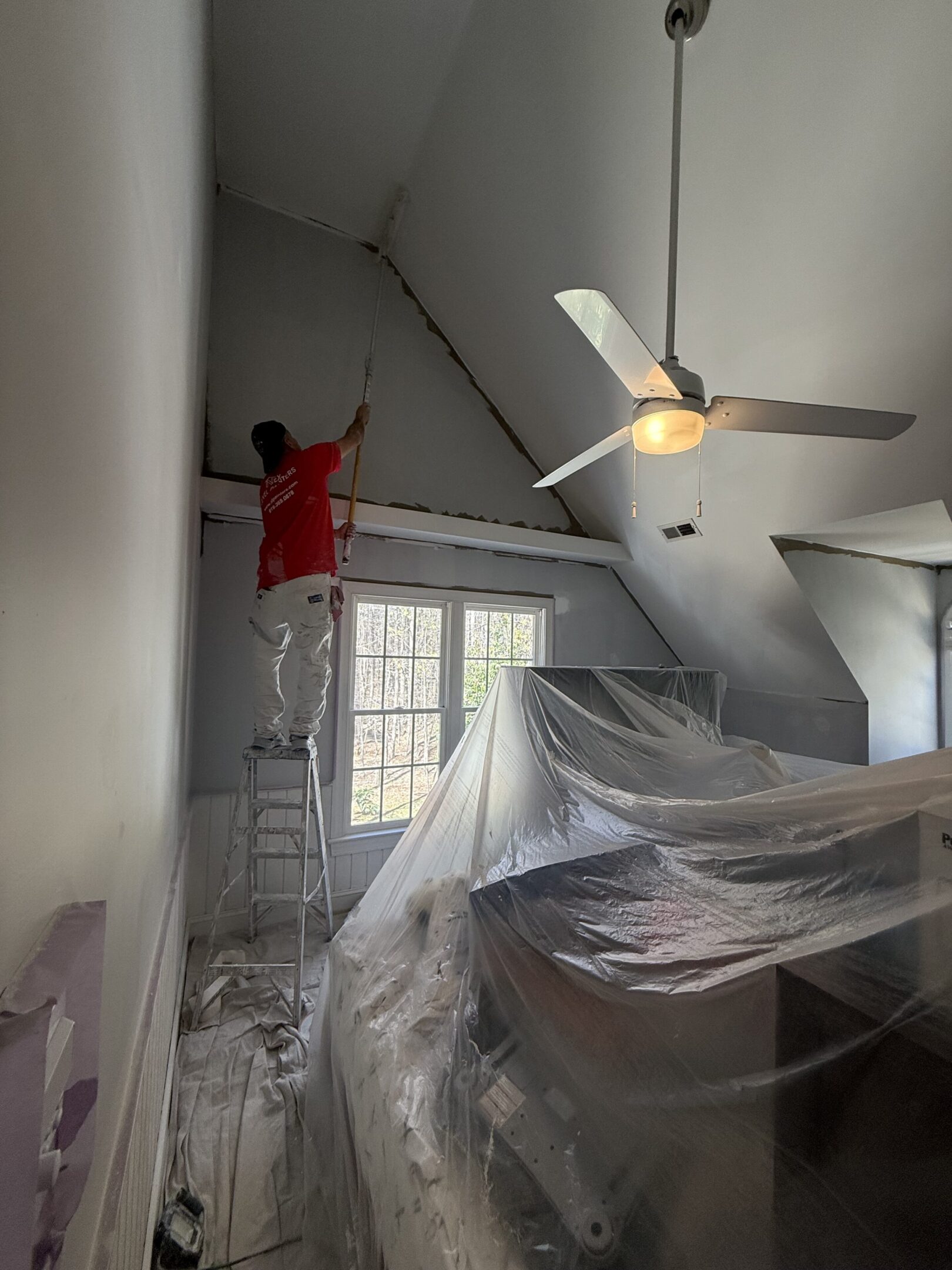 Person painting a tall wall in a room covered with protective sheets.
