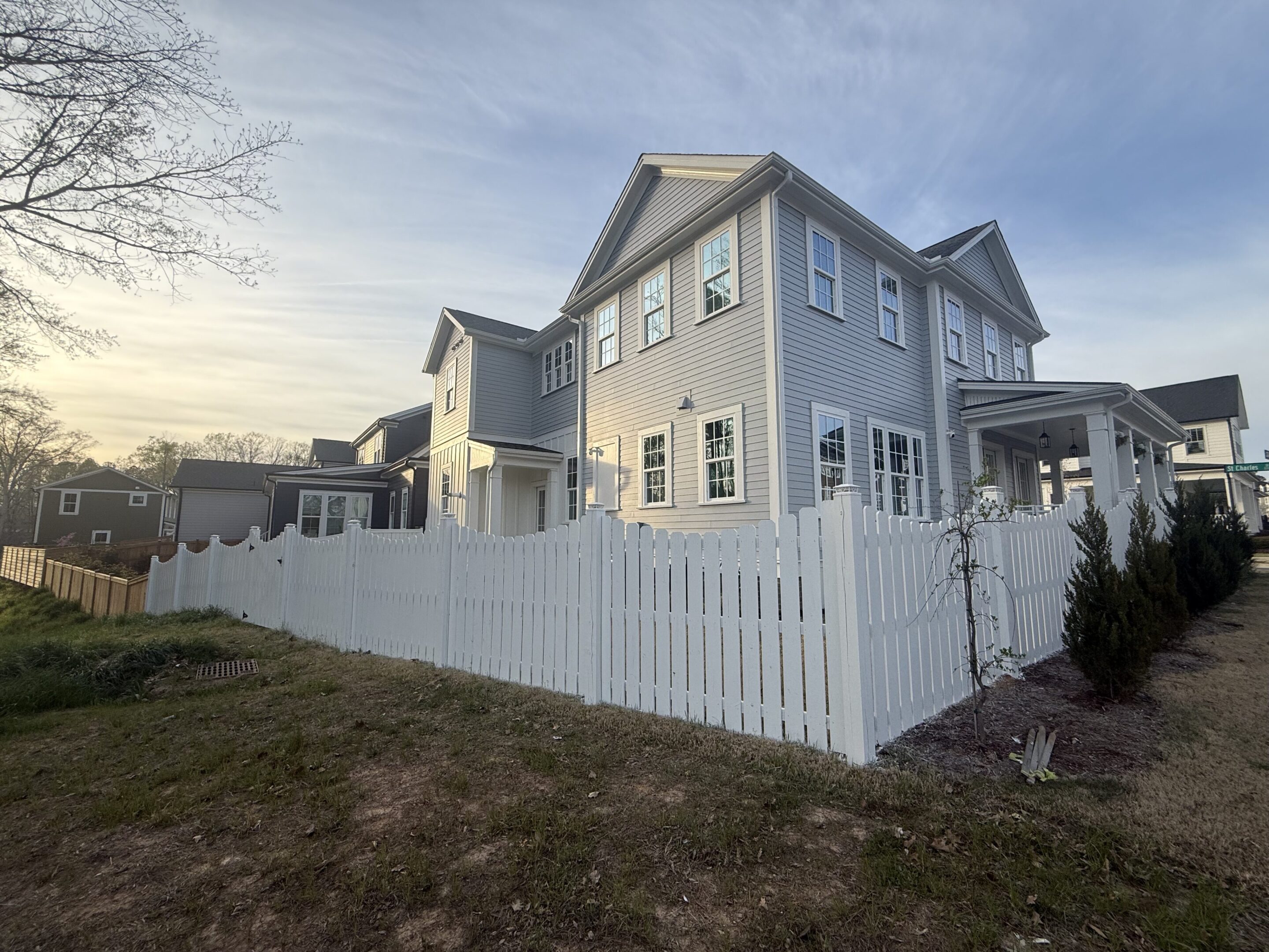 Two-story gray house with white trim and a white picket fence at sunset.