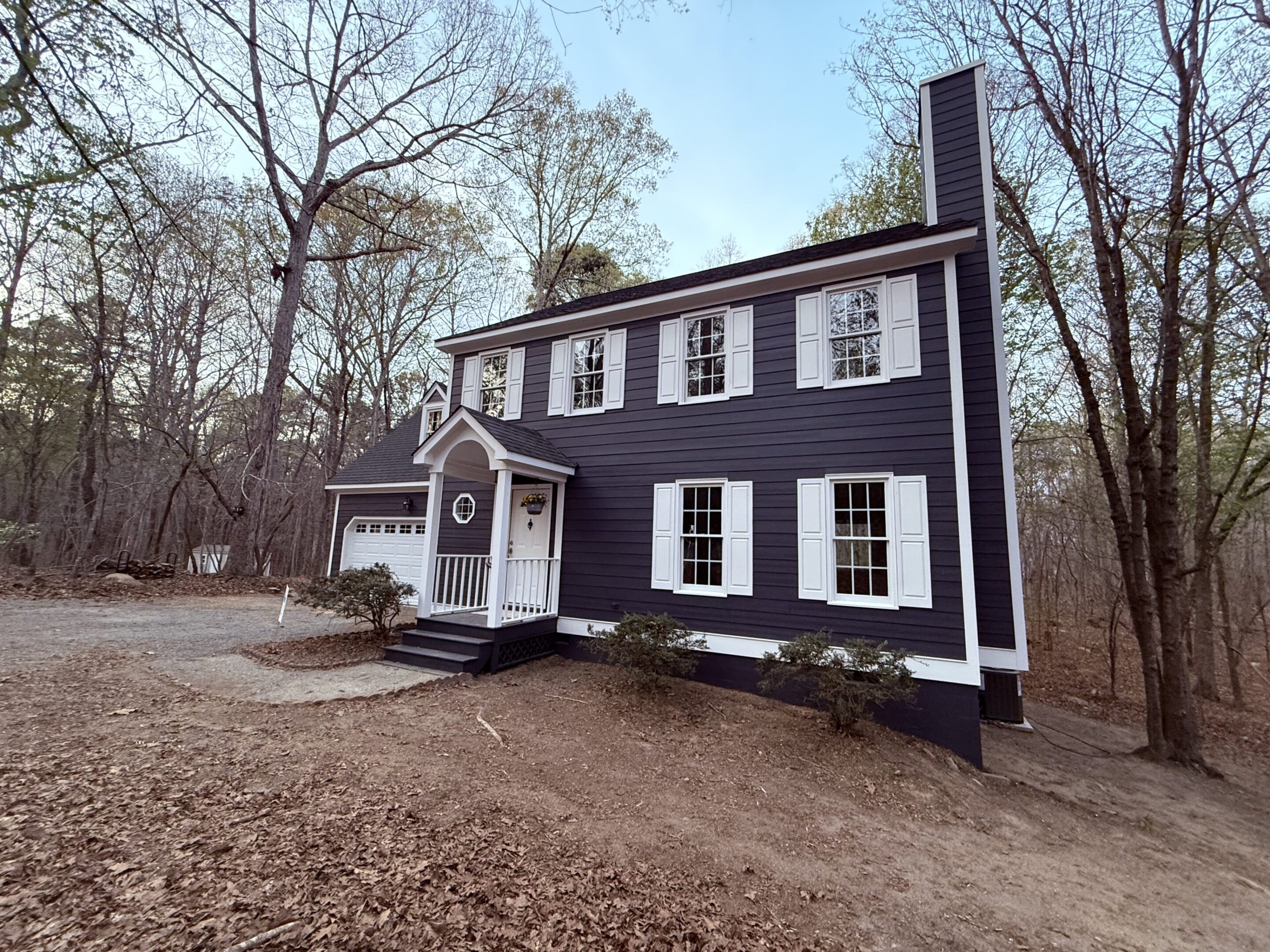 Charming two-story black house with white trim in a wooded area.