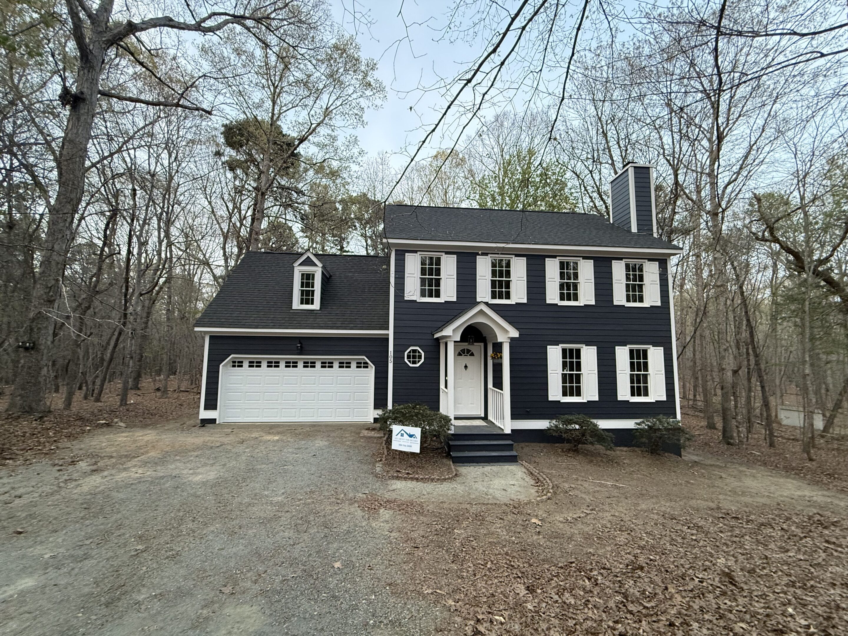 A two-story black house with white trim and a surrounding wooded area.