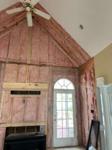 Interior wall with exposed pink insulation and a large arched window.