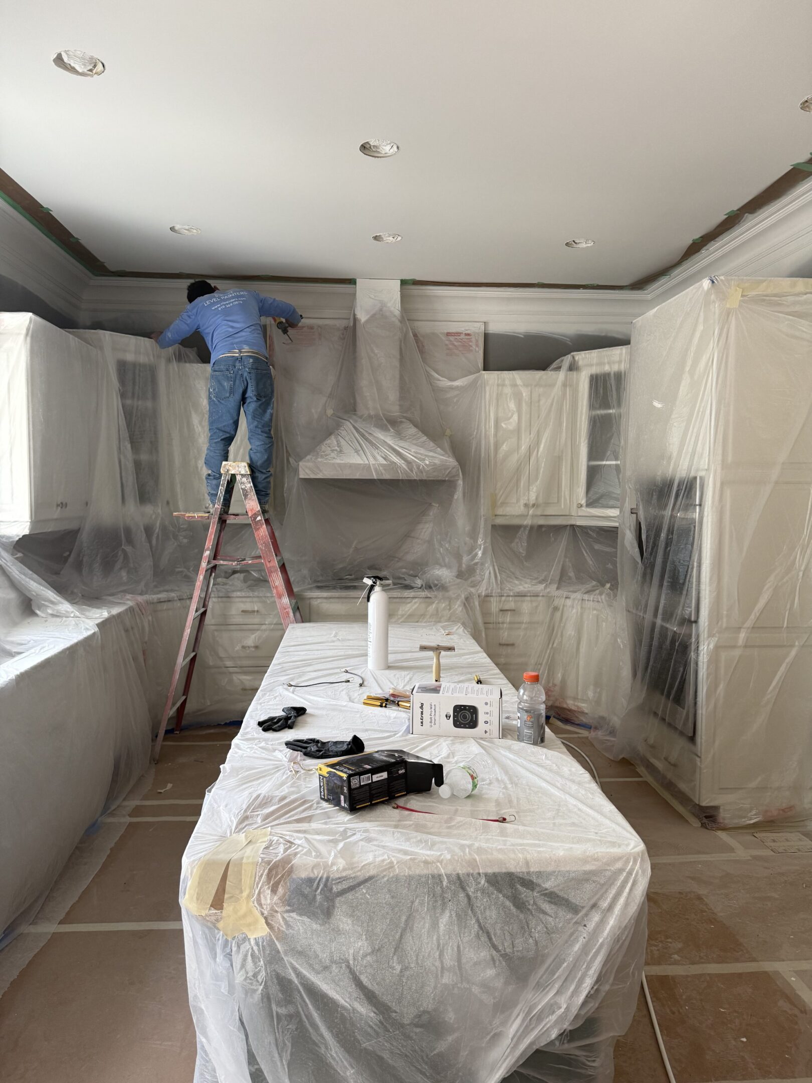 Kitchen being renovated with cabinets and appliances covered in plastic.