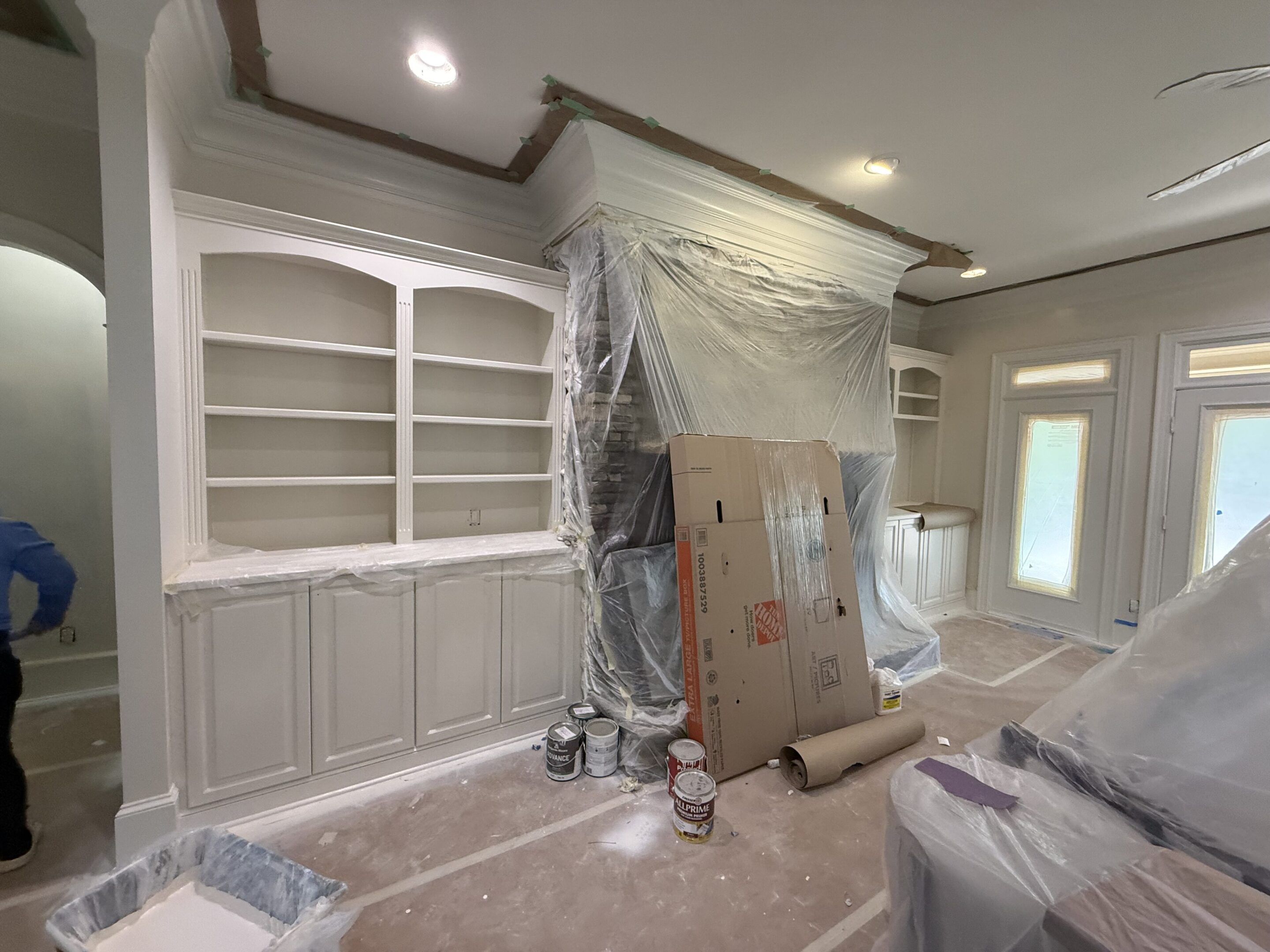Room under renovation with built-in shelves and plastic-covered area.