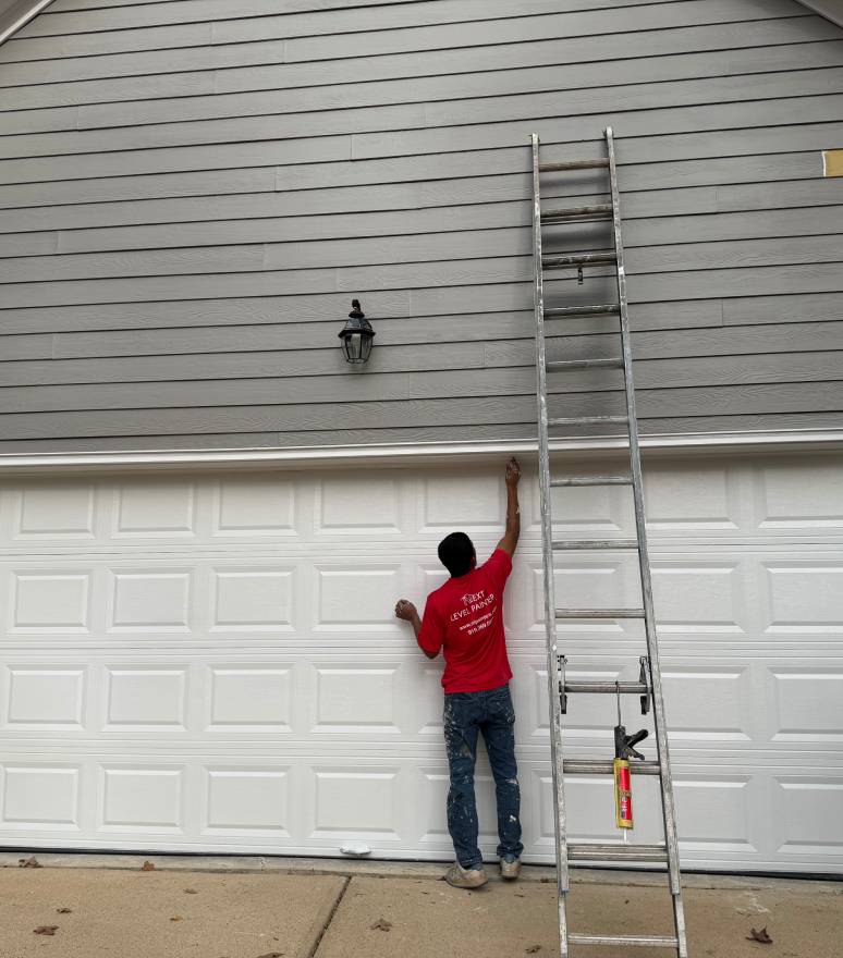Person in red shirt reaching up near a tall ladder by a garage door.
