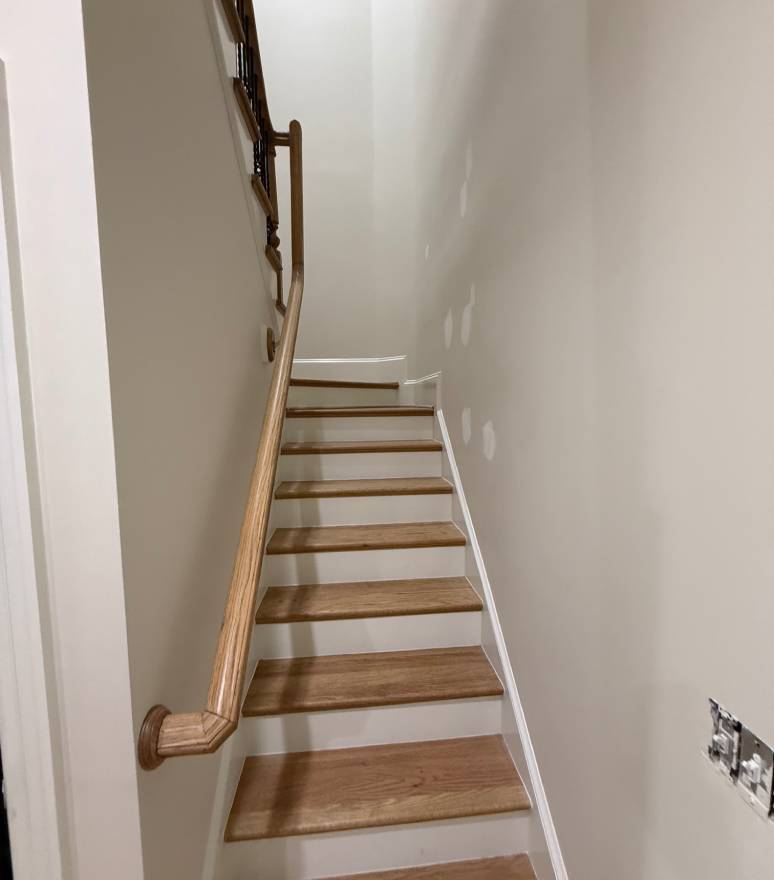 Narrow staircase with a wooden handrail and white walls.
