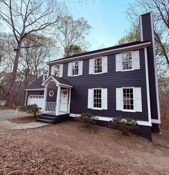 A charming black two-story house with white-trimmed windows surrounded by bare trees.