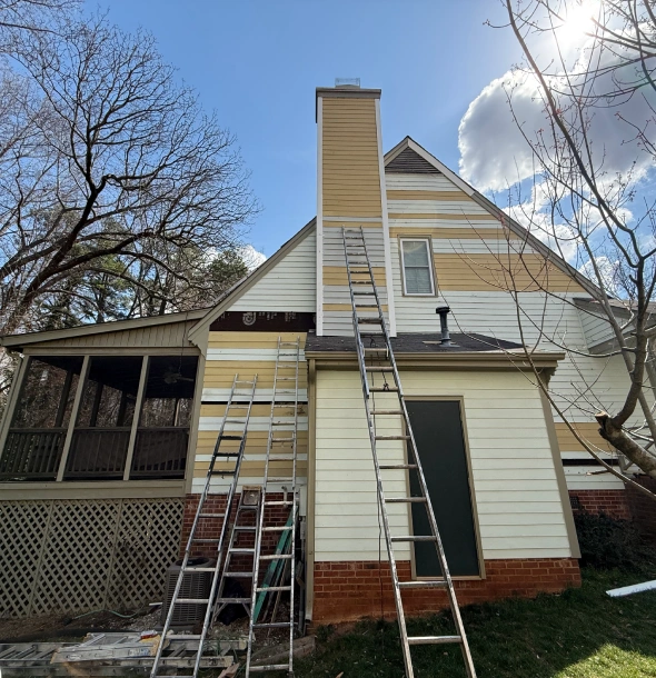 Two ladders leaning against a house with a cloudy sky.