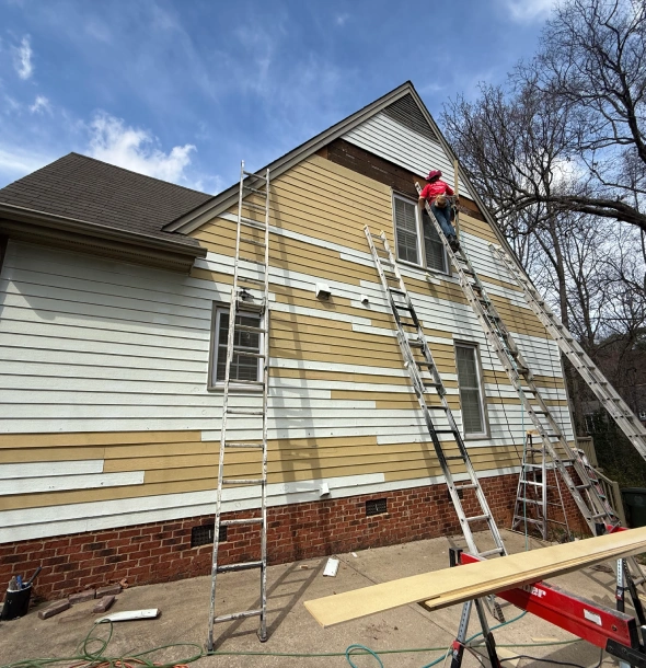 Workers installing siding on a house using ladders and scaffolding.