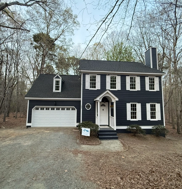 A dark blue two-story house with white trim and a two-car garage.