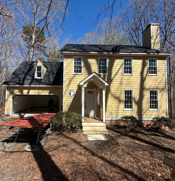 A yellow two-story house with a porch and a red car parked in the driveway.