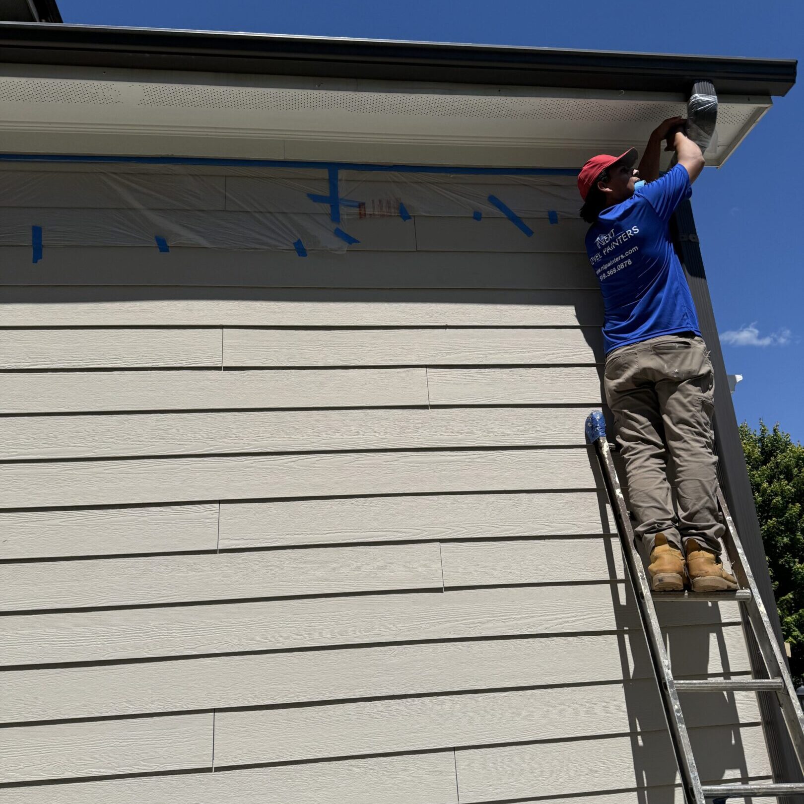 Man on ladder painting the exterior of a building under clear blue sky.