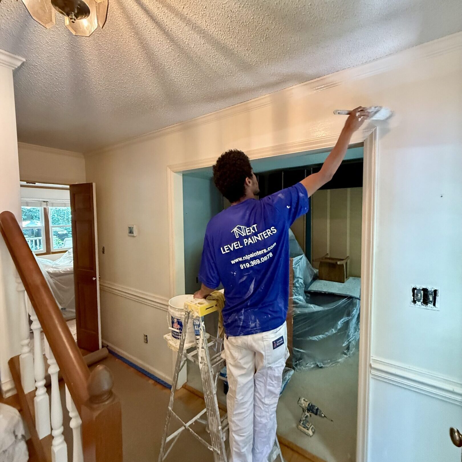 Painter working on white trim in a well-lit room.