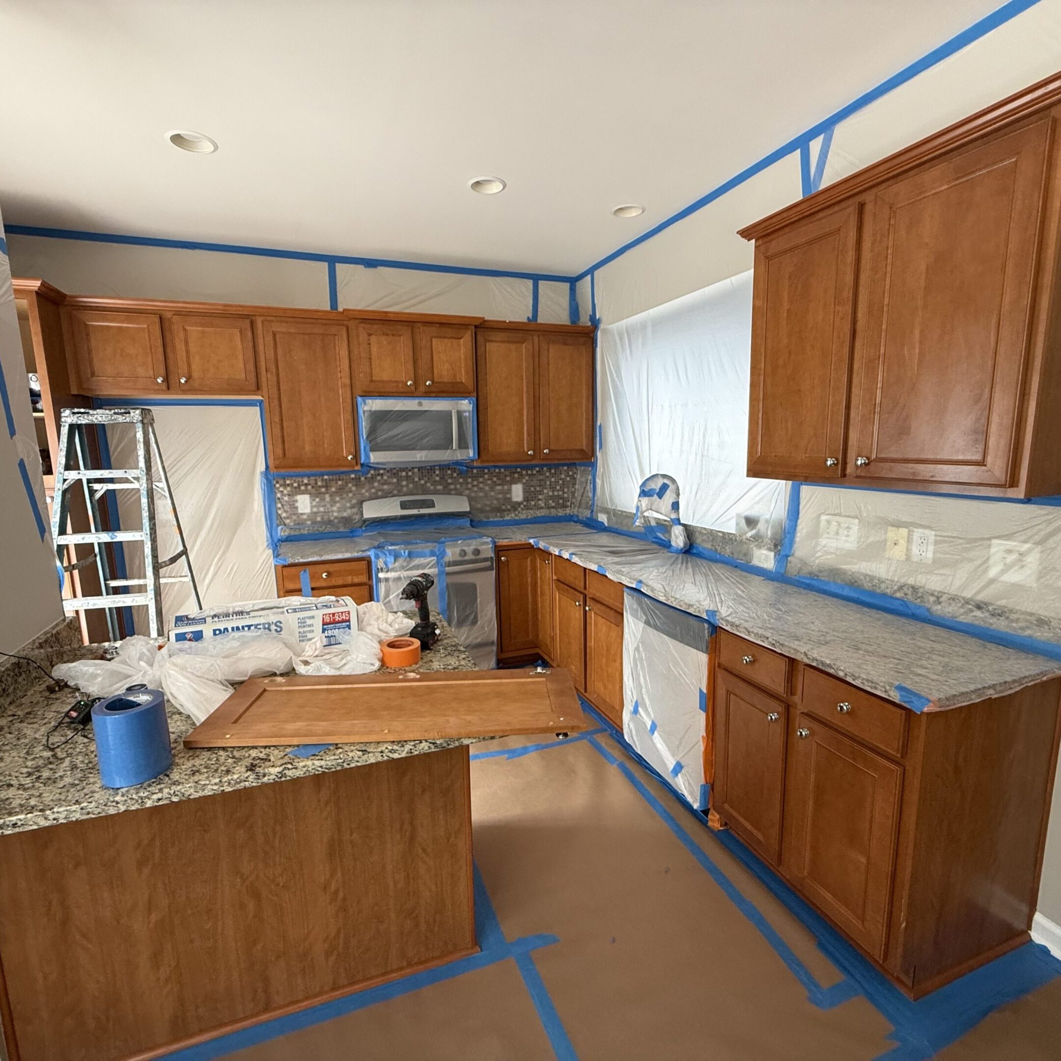 Kitchen under renovation with wooden cabinets and taped floors.