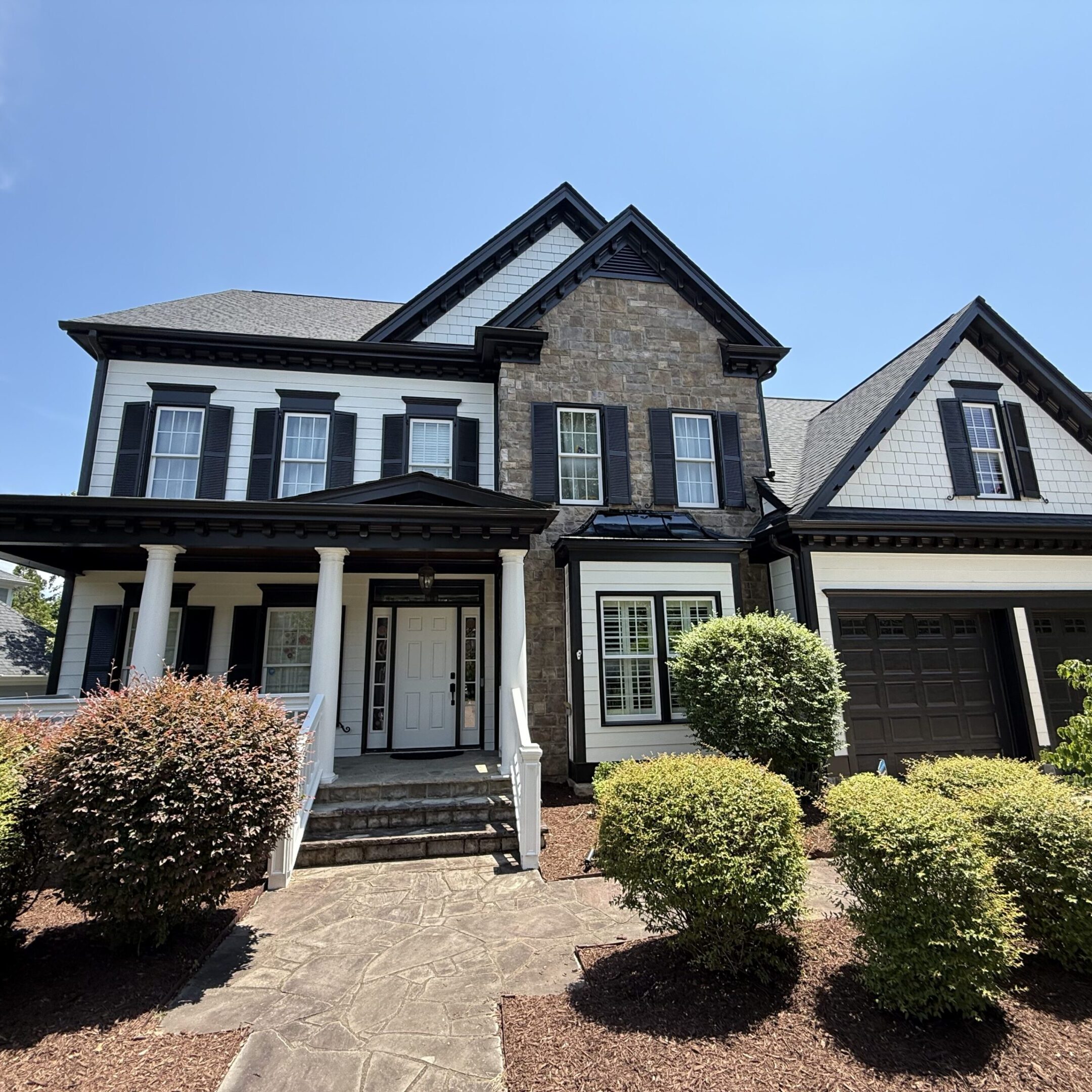 Elegant two-story house with stone facade and manicured shrubs.